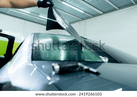 close-up of a car mechanic carefully sticking a protective tinted film on car glass detailing Royalty-Free Stock Photo #2419266103