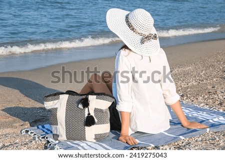 Young woman with stylish bag sitting on beach