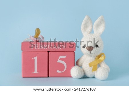 Toy bunny with golden ribbon, calendar and pacifier on blue background. Childhood cancer awareness concept