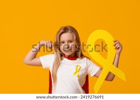 Cute teenage girl in superhero costume with yellow ribbon on color background. International Childhood Cancer Day Royalty-Free Stock Photo #2419276691
