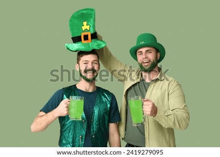 Happy young men in leprechaun hats with green beards holding glasses of beer on green background. St. Patrick's Day celebration