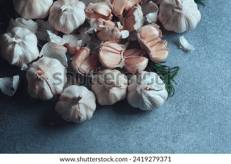 Garlic Bulbs and Cloves Composition on Dark Texture. Overhead view of garlic bulbs and individual cloves, complemented by rosemary, on a dark textured surface.
