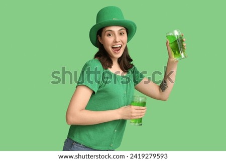 Happy young woman in leprechaun hat with glasses of beer on green background. St. Patrick's Day celebration