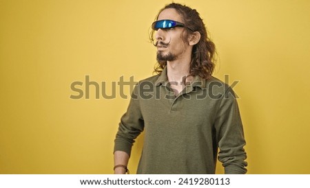 Young hispanic man playing video game using virtual reality glasses over isolated yellow background