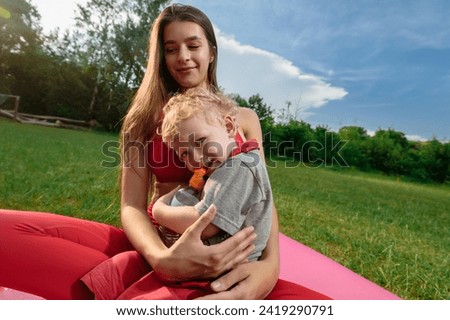Young happy mother and her cute little son having outdoor workout in park, Warm family yoga: A young woman, child, and family stretch together in the comforting park ambiance