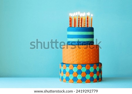 Brightly colored birthday cake covered with fondant, three tiers and colorful birthday candles