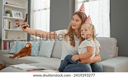 Caucasian mother and daughter making heartwarming birthday memories, hugging and taking a captivating self-picture together with a smartphone, from their cozy living room sofa.
