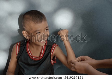 Asian boy smiling cheerfully with someone nursing a wound on his arm caused by an accident a view from above on a background of a gray wall and beautiful bokeh sunlight.