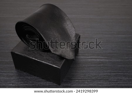 Black tie rolled on black gift box close up view, Black on black concept, Copy space, Single object  Royalty-Free Stock Photo #2419298399