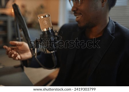 Close up shot of gold steel net microphone and African American male podcaster speaking during podcast in studio