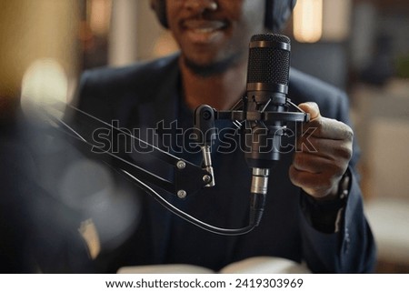 Close up shot of professional condenser microphone and African American male hand setting it up during live podcast in studio