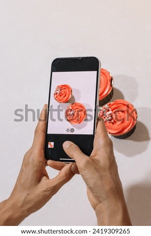 Woman's hand taking a cell phone picture of cupcakes decorated w