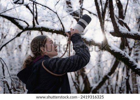 Young woman outside photographer wearing warm clothes and takes pictures of winter in a snowy park, enthusiastic girl looking up and makes photo on digital camera in the winter forest, travel, hobby