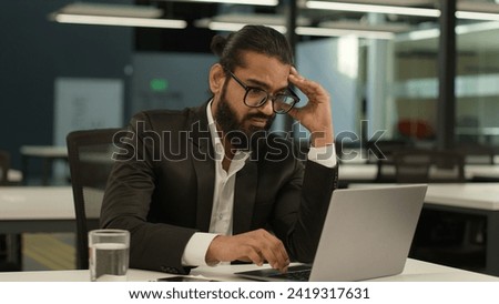 Bored Arabian business man at office table tired Indian clerk businessman worker sad dissatisfied disinterest manager employer boredom at workplace indoors laptop computer typing exhausted boring job