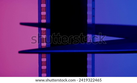 Scissors cuts a strip of photographic film on a blue and pink background close up.