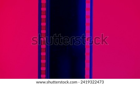 Vertical film strip on a red background, close up. 35mm film slide frame. Long, retro film strip frame. Copy space. Royalty-Free Stock Photo #2419322473