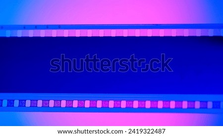 Blank undeveloped strip of film on blue background, illuminated by pink neon light in close up. 35mm film slide frame. Cinema or photo frames. Long, retro film strip frame. Copy space.