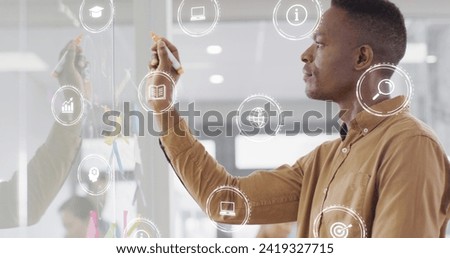Image of financial data with icons over african american businessman writing on whiteboard. Global business, finances, computing and data processing concept digitally generated image.