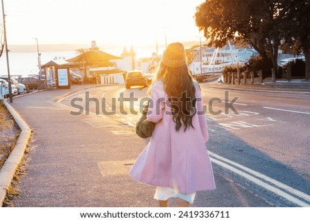 Back view stylish hipster woman with color hair walking the street at sunset wearing pink coat, knitted hat and fur bag, happy mood, seasonal fashion style. Barbiecore style trend. Selective focus. Royalty-Free Stock Photo #2419336711