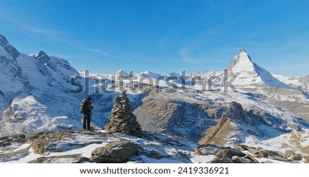 Panoramic landscape of Young man backpacker take a photo by camera at Switzerland mountain peak view point with iconic famous landscape Matterhorn background. Nature, Travel and Adventure concept.