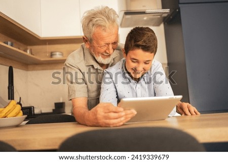 Smiling grandfather and grandson watching video on tablet PC at home