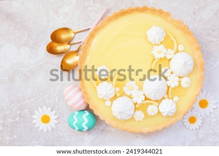 Spring lemon tart with white chocolate flowers and meringue. Easter dessert concept. Above view table scene over a bright stone background.