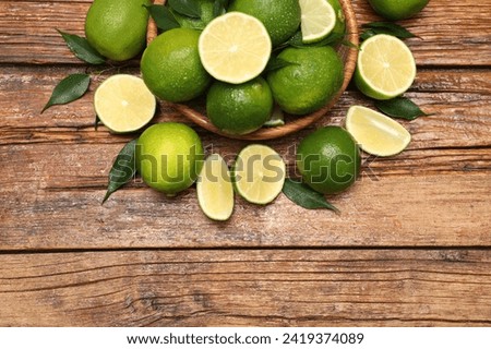 Fresh limes and green leaves with water drops on wooden table, flat lay. Space for text