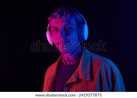 Portrait of smiling young man in headphones standing in neon light and listening to music