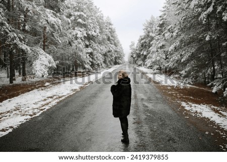 beautiful woman standing on the road with a view of the snowy forest. a woman in a fur black fur coat in winter in the forest. middle-aged woman winter photo shoot