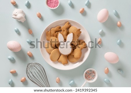 Easter homemade glazed bunnies shaped cookies, pink eggs in white plate on blue background. Greeting card with space for text. Top view. Festive food and snacks.