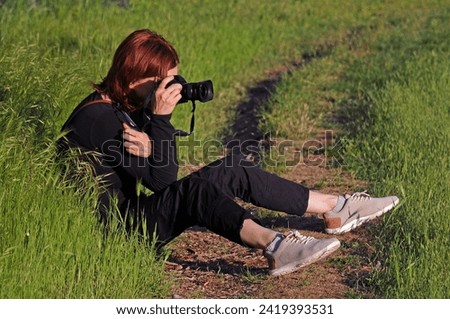Unidentifued woman takes pictures sitting on the grass