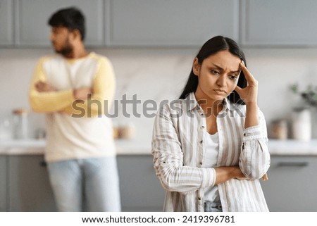 Selective focus on upset young indian woman touching her head, have fight with husband or boyfriend, modern kitchen interior. Millennial eastern couple have difficulties in marriage. Divorce, breakup Royalty-Free Stock Photo #2419396781