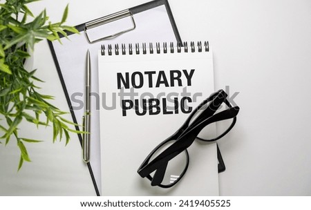 A professional arrangement of notary public supplies, including eyeglasses, a notebook, a clipboard, and a pen on a white table with a green plant. Ideal for stock agencies.