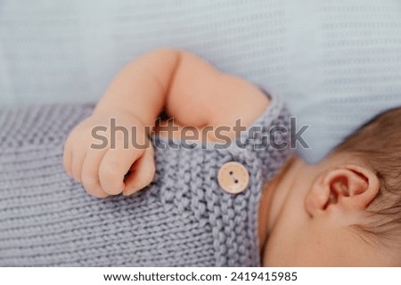 two weeks old baby, close-up,  baby's hand, ear, shoulder, little fingers, first dark hair, grey knitted wool suit, button, tiny fingers, newborn, boy, 2 weeks old, laying, no face, details Royalty-Free Stock Photo #2419415985