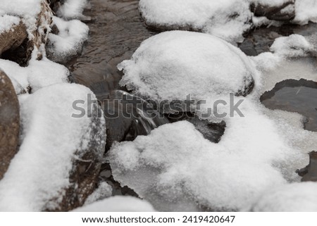 a small river covered with snow and ice in winter, the unfrozen part of the river in winter during snowfall