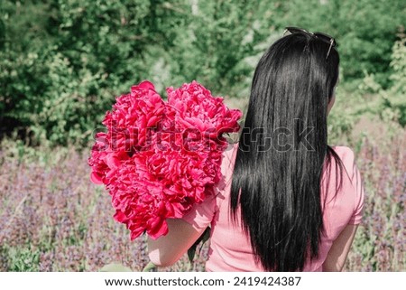Brunette in a field with a bouquet of burgundy peonies. 