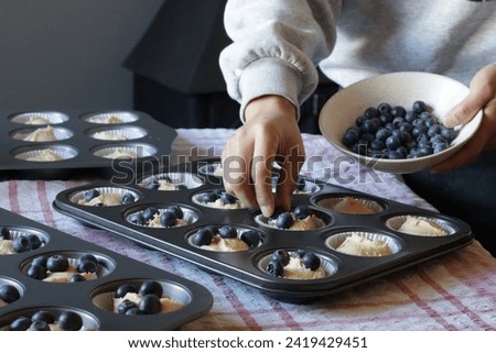 Blueberry muffin cup cake homemade. Woman hand put fresh blueberry on top of cake. Family lifestyle home cooking concept. Fireplace background.