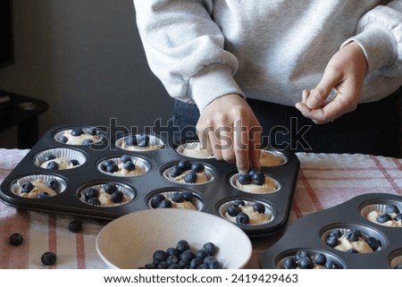 Blueberry muffin cup cake homemade. Woman hand put fresh blueberry on top of cake. Family lifestyle home cooking concept. Fireplace background.