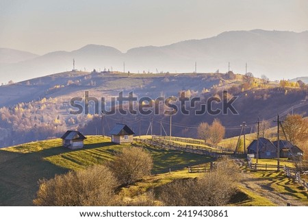 Panoramic view of misty sunny autumn evening in mountains. Beautiful sunset hills landscape. Slopes, meadows, fields, village, house, dirt road. Amazing fall rural scene. Carpathian range. Ukraine