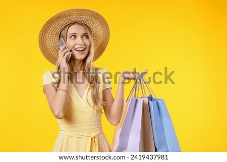Photo of cheerful young woman excited talking by mobile phone standing isolated over yellow background with shopping bags. Consumerism, purchasing goods, Black Friday concept