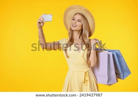 Amazing young woman posing isolated over yellow background holding shopping bags take selfie by mobile phone. Influencer vlogger blogger posting on social media Royalty-Free Stock Photo #2419437987