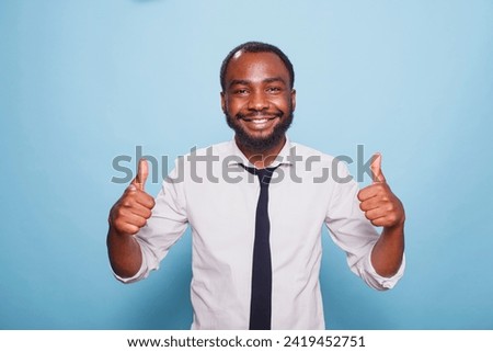 African American man is portrayed in front of the camera giving thumbs up with both his hands. Smiling black person spreading positivity, feeling joy and excitement and offering approval. Royalty-Free Stock Photo #2419452751