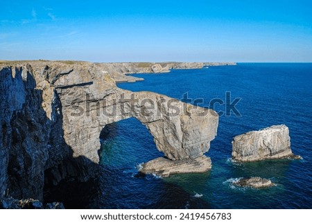 Natural rock arch known as The Green Bridge of Wales on the coast of Pembrokeshire, UK. Blue water and cliff landscape Royalty-Free Stock Photo #2419456783