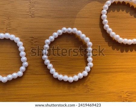 White pearl beaded bracelets. Three simple bracelets with plastic beads on wooden table. Trendy minimalist luxury fashionable design. Perfect visual for advertisement business catalogue idea