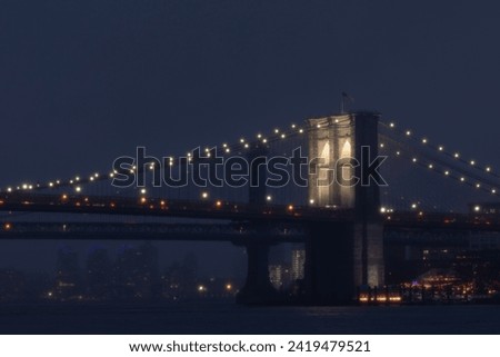Foggy evening view of the Brooklyn Bridge illuminated at night.