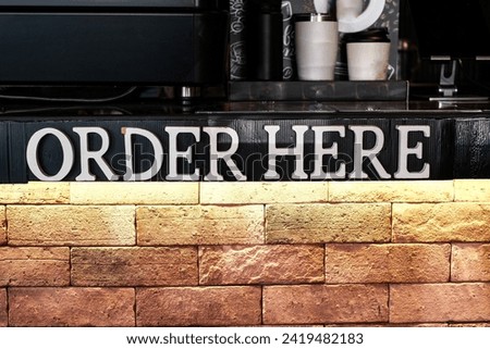 A sign that says “ORDER HERE” on a brick wall