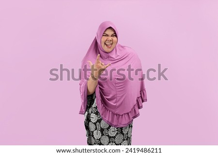 Expression of asian woman shows rock on, heavy metal horns gesture, having fun, enjoying concert or festival, pink background.