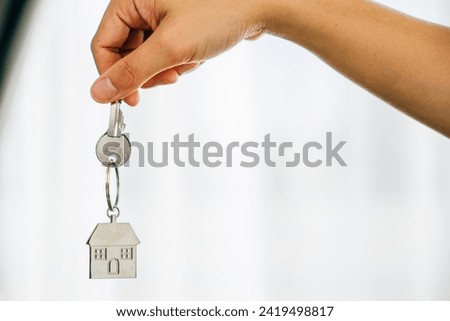 Woman's hand with house key denoting achievement in homeownership. Agent showcases model home symbolizing real estate success. Confidence and happiness prevail.