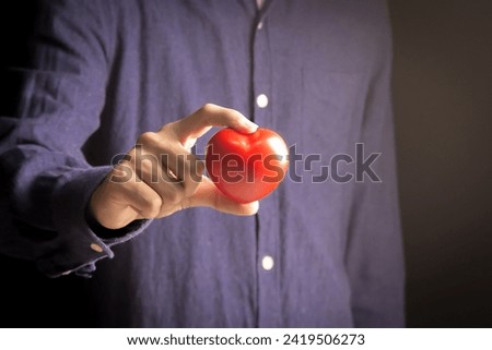 Close-up of a man's hand holding a red heart symbol,stock photography concept.