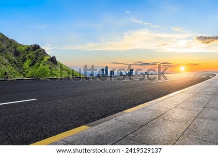 Asphalt highway road and green mountain with city skyline at sunset